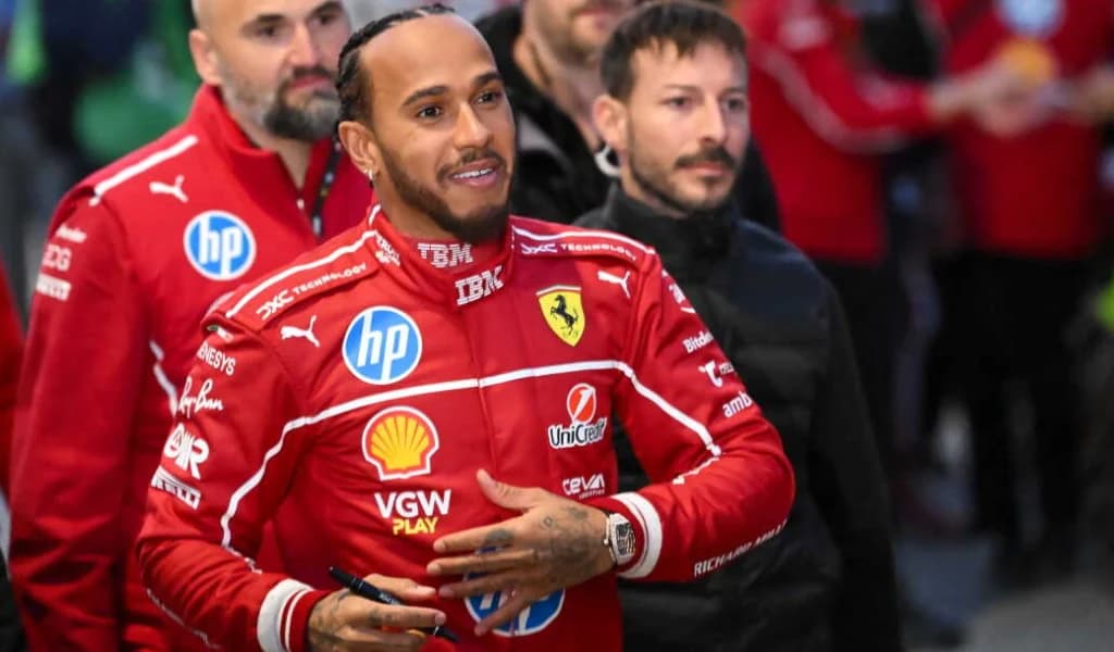 Lewis Hamilton in Ferrari red smiles while greeting people in the paddock.