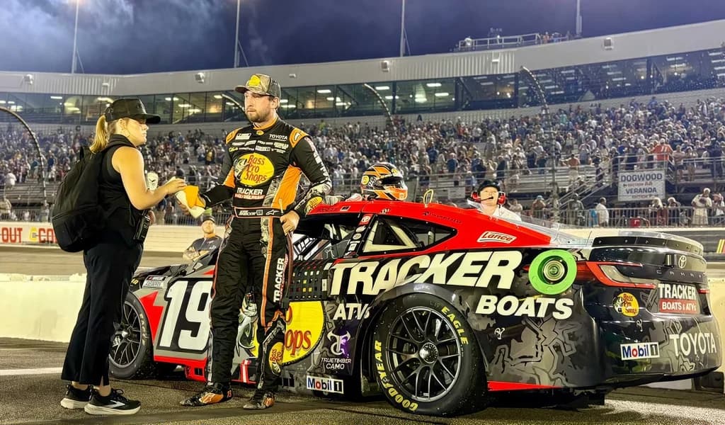 Driver stands beside the number 19 Bass Pro Shops car on pit road at night