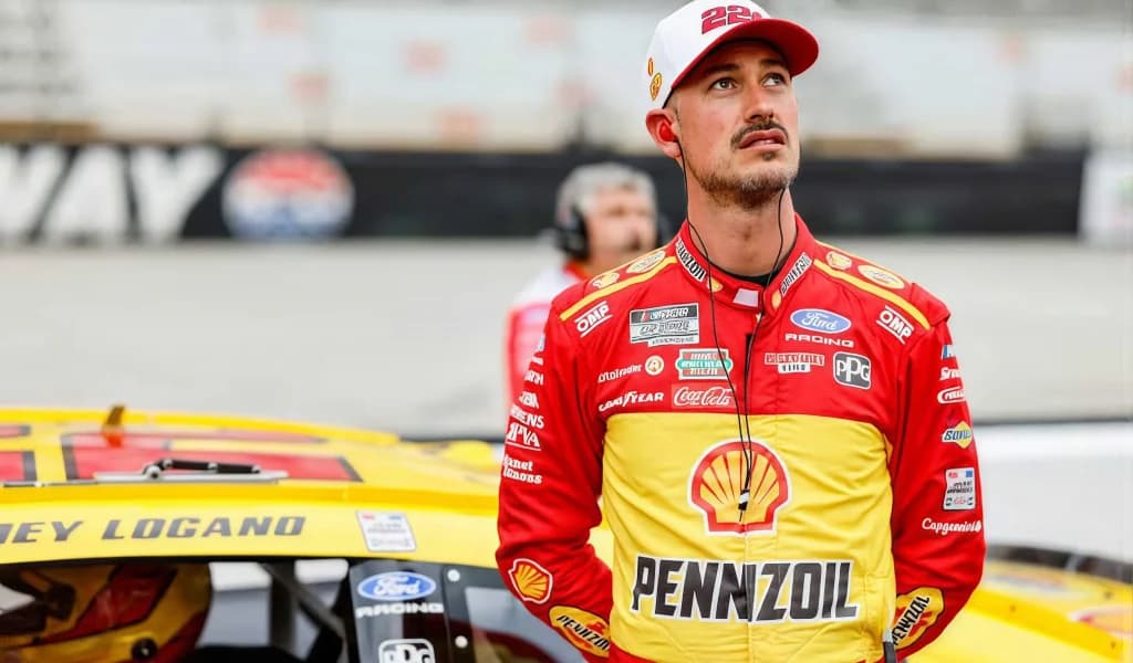 Joey Logano in his yellow Pennzoil firesuit stands beside his car on pit road.