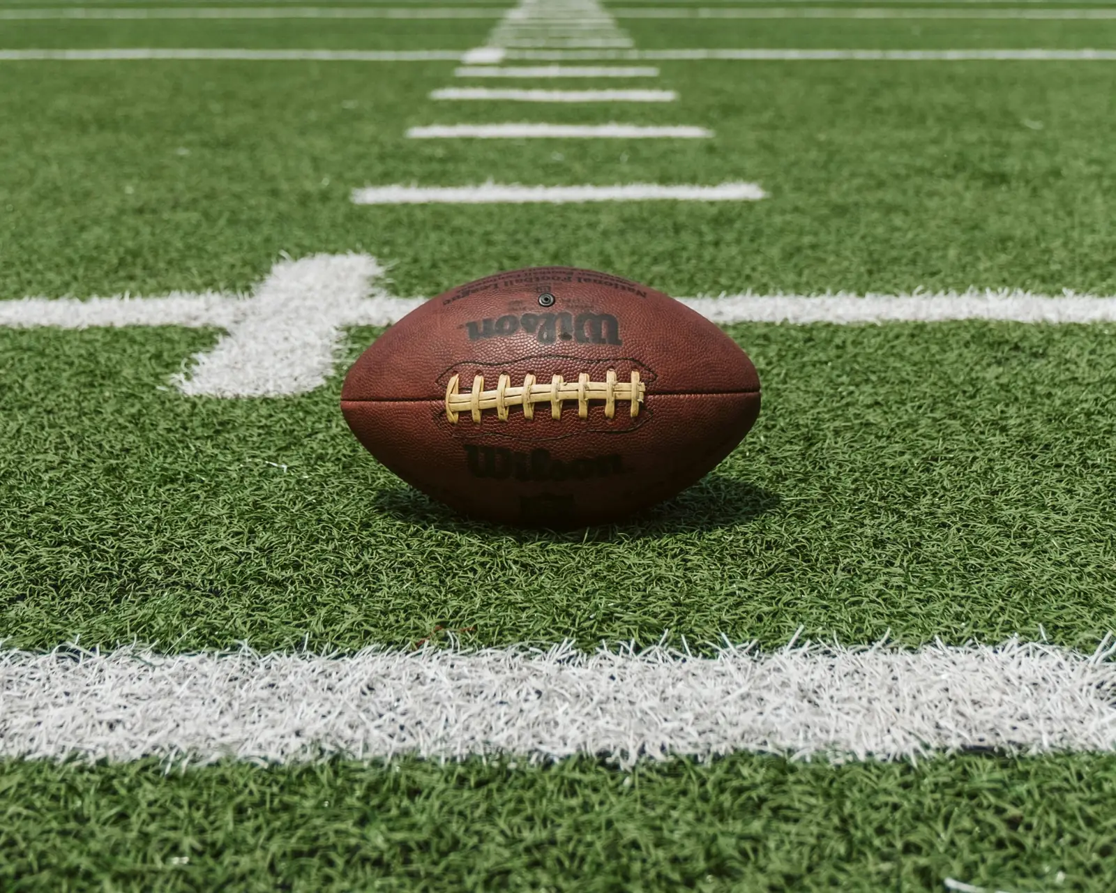 Football resting on the yard line of a turf field