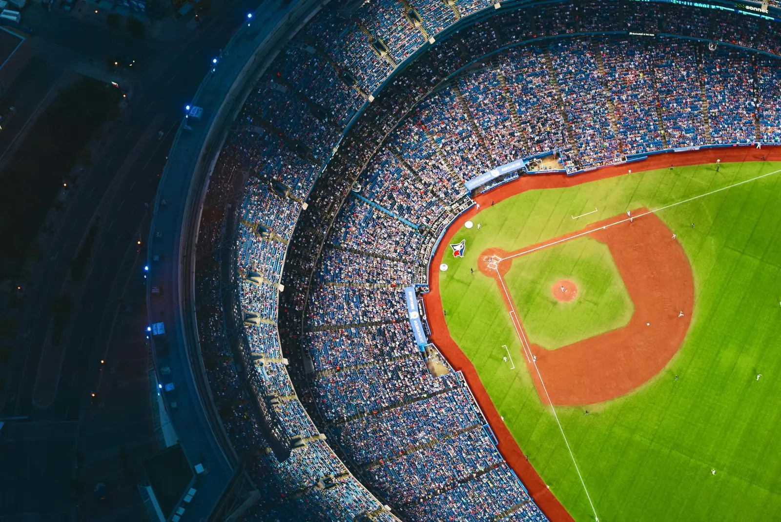 Aerial view of a packed baseball stadium at dusk with the infield lit below