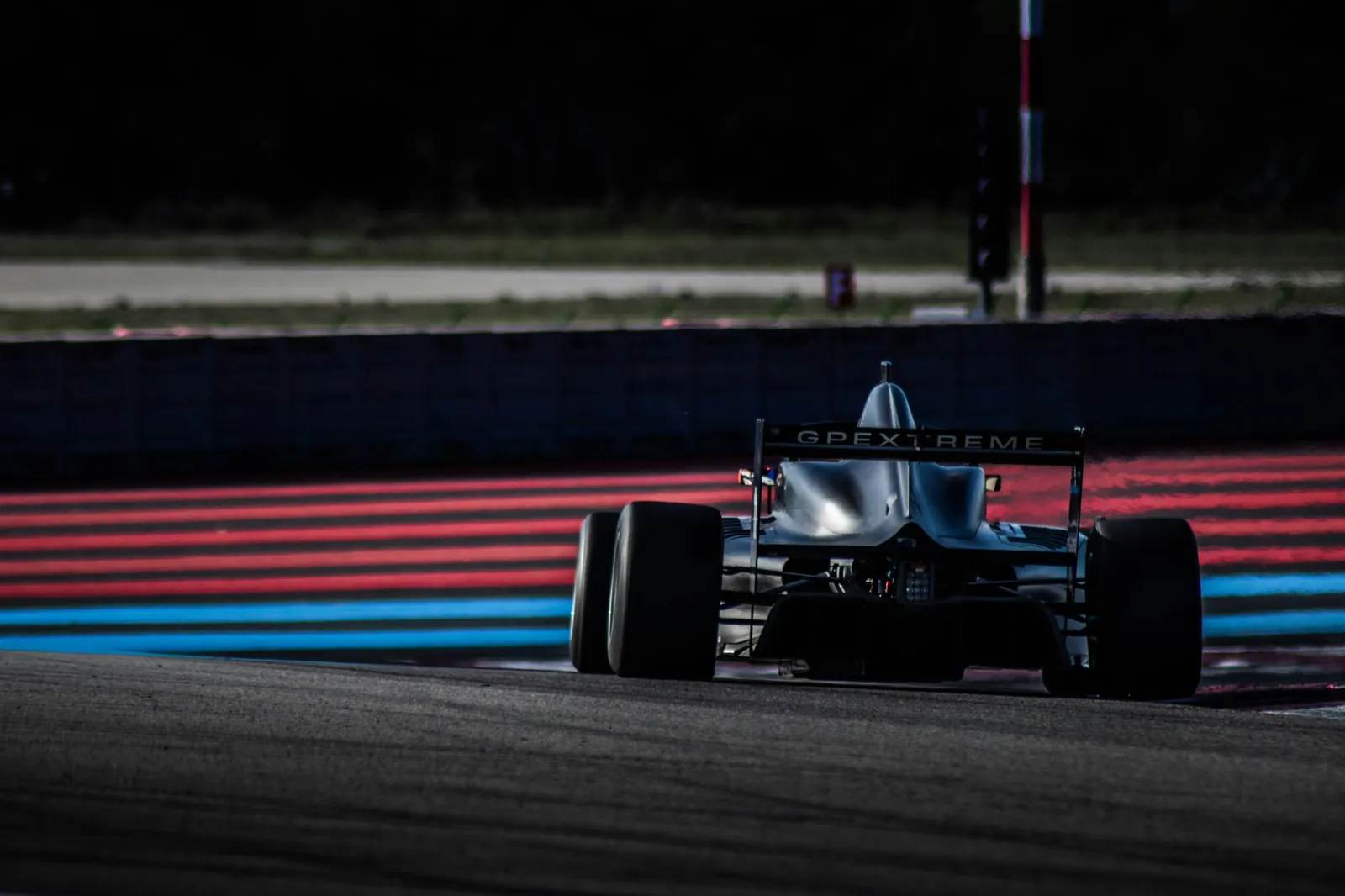 Single-seater race car cornering past red and blue run-off stripes